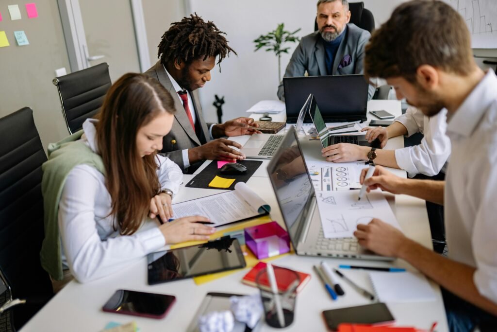Team of professionals collaborating around a table in a modern office, focusing on projects and discussions.